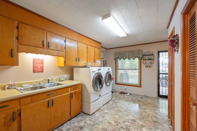 clothes washing area featuring cabinets, crown molding, washing machine and clothes dryer, and sink