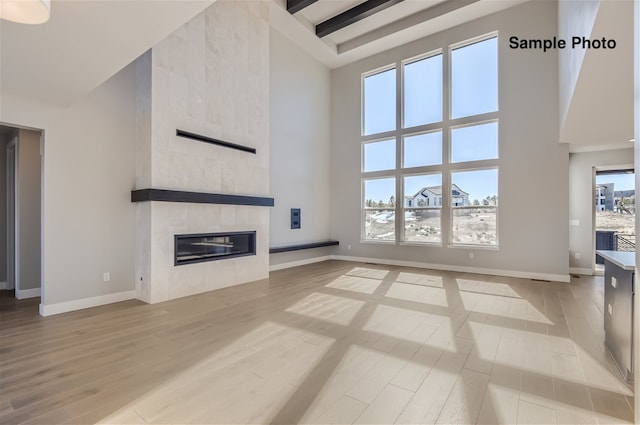 unfurnished living room featuring a towering ceiling, beamed ceiling, light hardwood / wood-style floors, and a tile fireplace