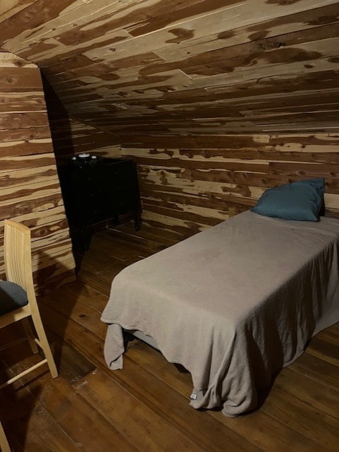 bedroom featuring wooden walls, vaulted ceiling, and dark wood-type flooring