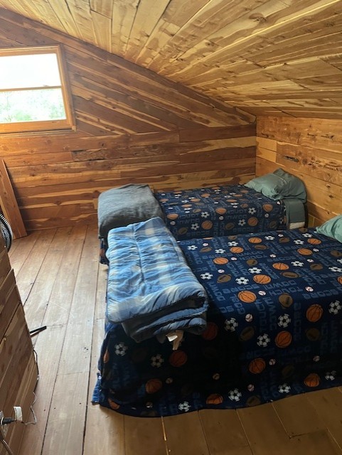 unfurnished bedroom with wood-type flooring, wooden walls, vaulted ceiling, and wooden ceiling