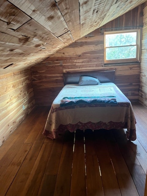 unfurnished bedroom featuring wooden walls, dark wood-type flooring, and vaulted ceiling