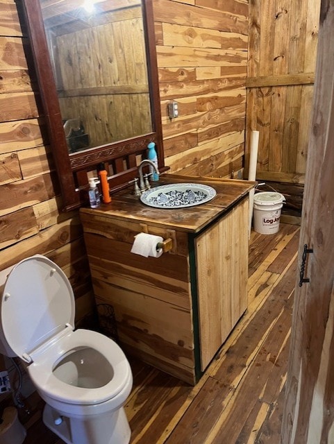 bathroom featuring vanity, wood walls, hardwood / wood-style floors, and toilet