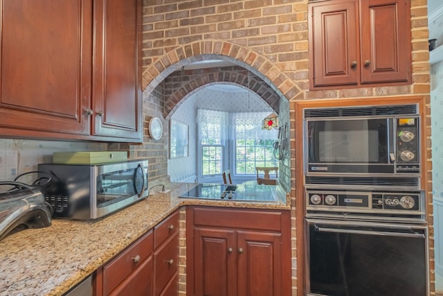 kitchen with light stone counters, black appliances, and brick wall