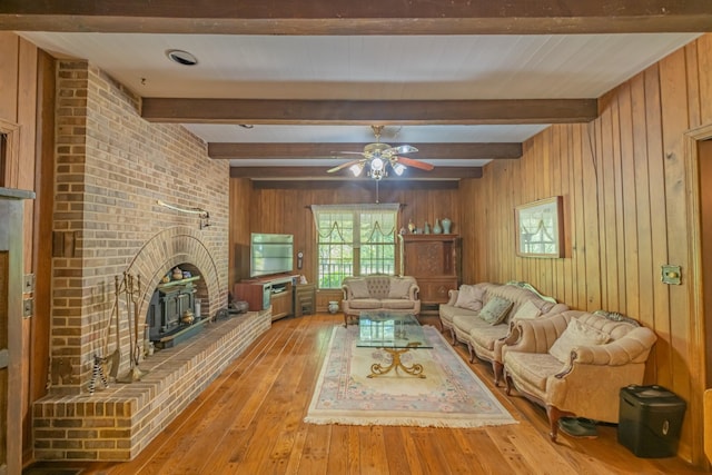 unfurnished living room featuring a brick fireplace, a ceiling fan, beamed ceiling, wood walls, and hardwood / wood-style floors