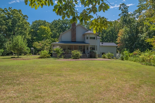 back of house featuring a chimney, covered porch, and a lawn
