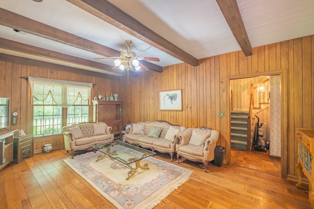 living room with ceiling fan, wooden walls, beam ceiling, and light hardwood / wood-style floors