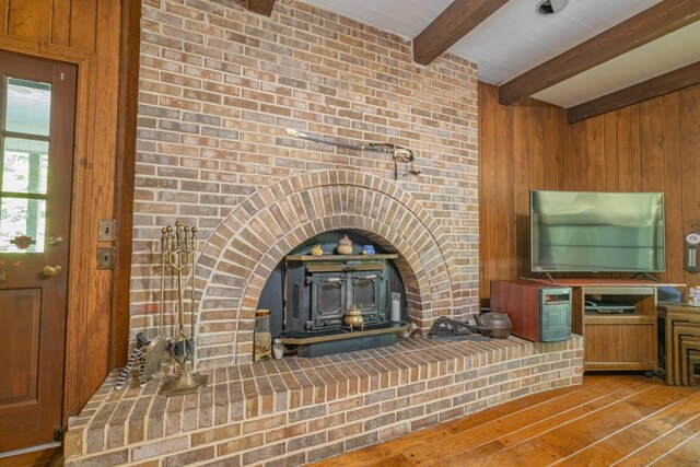 unfurnished living room featuring wood walls, wood finished floors, a wood stove, and beamed ceiling