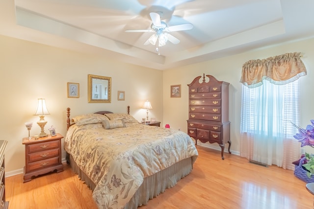 bedroom featuring light wood-type flooring, a tray ceiling, and ceiling fan