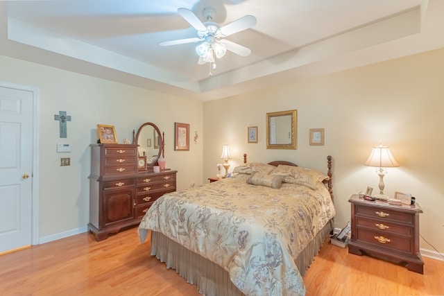 bedroom featuring light hardwood / wood-style floors, ceiling fan, and a raised ceiling