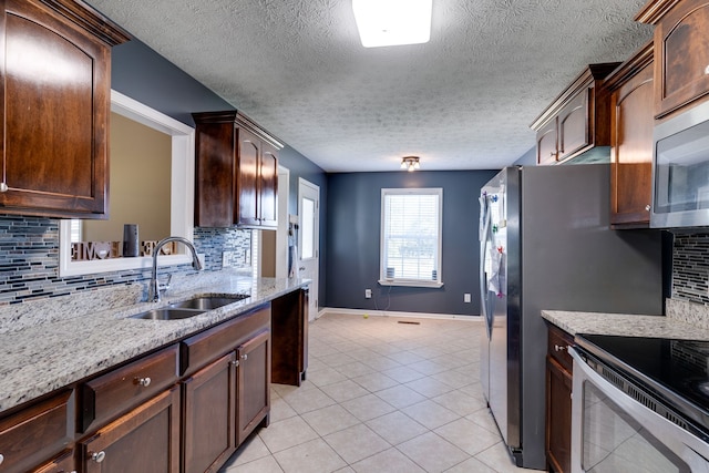 kitchen featuring light tile patterned flooring, backsplash, stainless steel appliances, a textured ceiling, and sink