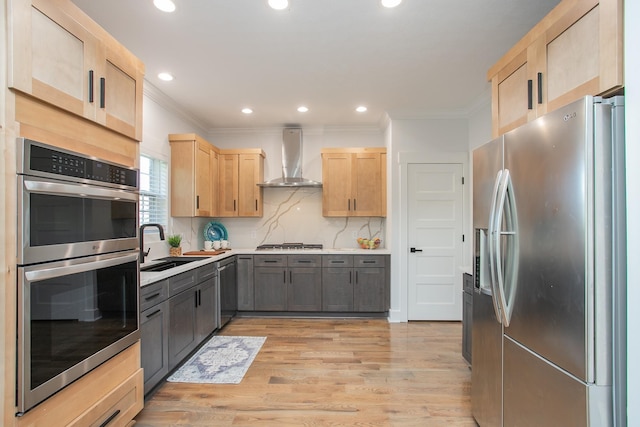 kitchen featuring light wood-type flooring, wall chimney range hood, gray cabinetry, appliances with stainless steel finishes, and light brown cabinetry