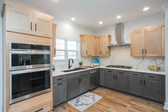 kitchen with gray cabinetry, wall chimney exhaust hood, stainless steel appliances, light brown cabinetry, and light hardwood / wood-style flooring