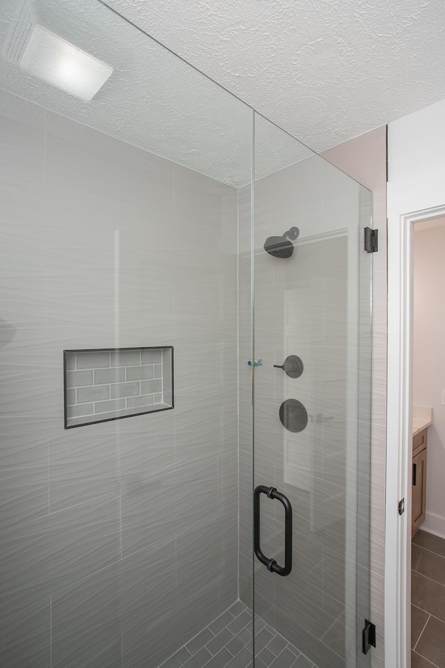 bathroom featuring a textured ceiling, a shower with door, vanity, and tile patterned floors