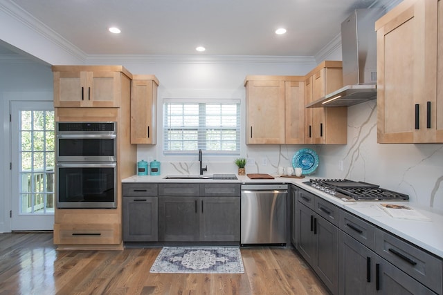 kitchen with gray cabinetry, stainless steel appliances, wall chimney range hood, and sink