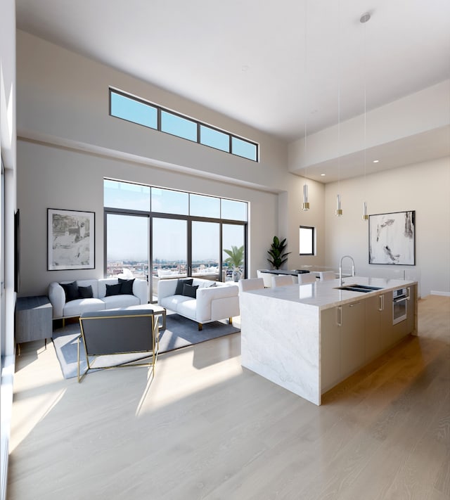 kitchen with light hardwood / wood-style floors, sink, a center island with sink, decorative light fixtures, and a high ceiling