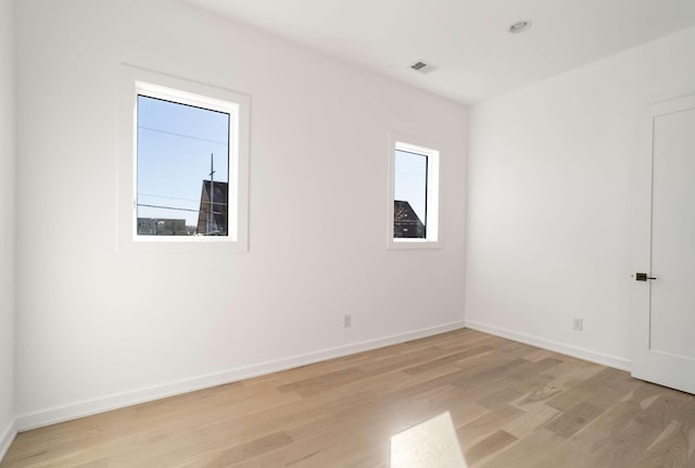 spare room featuring light wood-type flooring, visible vents, and baseboards