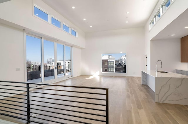 living room with recessed lighting, light wood-type flooring, baseboards, and a towering ceiling