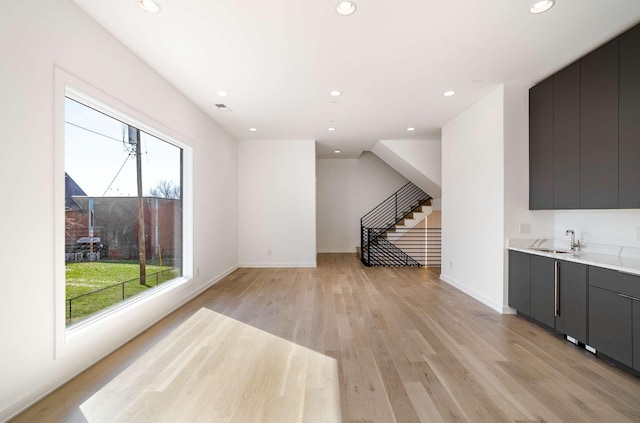 unfurnished living room featuring recessed lighting, stairs, light wood-style floors, and a sink