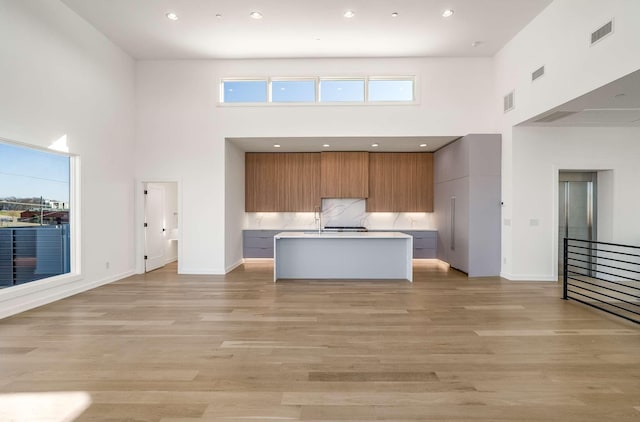 kitchen with light wood-type flooring, visible vents, modern cabinets, light countertops, and a towering ceiling