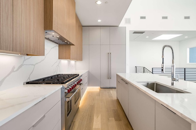 kitchen featuring a sink, double oven range, light stone countertops, and modern cabinets