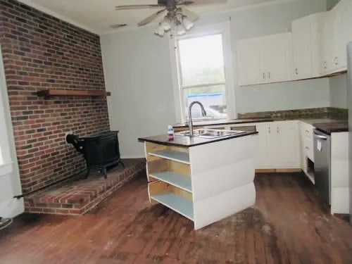 kitchen with a wood stove, dark hardwood / wood-style flooring, sink, and white cabinets