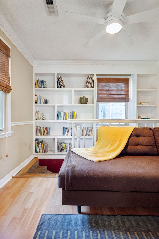 living area featuring a textured ceiling, crown molding, ceiling fan, built in shelves, and hardwood / wood-style floors