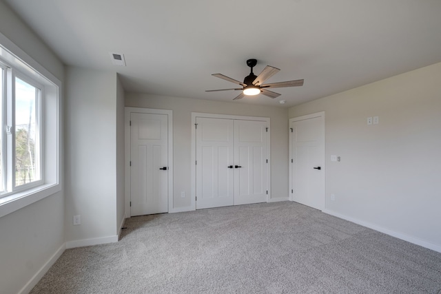 unfurnished bedroom featuring ceiling fan, two closets, light colored carpet, and multiple windows