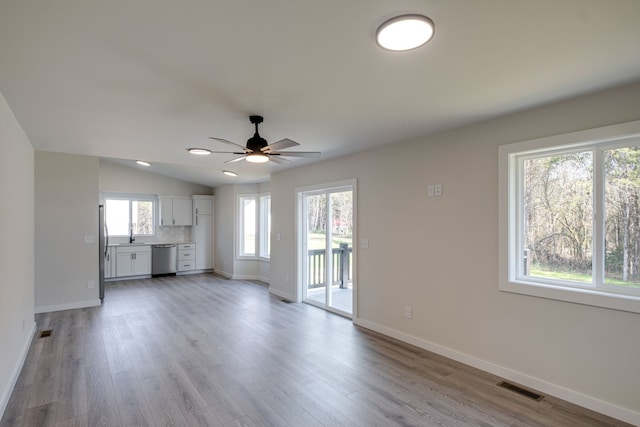 unfurnished living room featuring lofted ceiling, light wood-type flooring, ceiling fan, and a healthy amount of sunlight