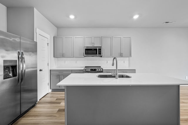 kitchen featuring stainless steel appliances, sink, a center island with sink, and gray cabinetry