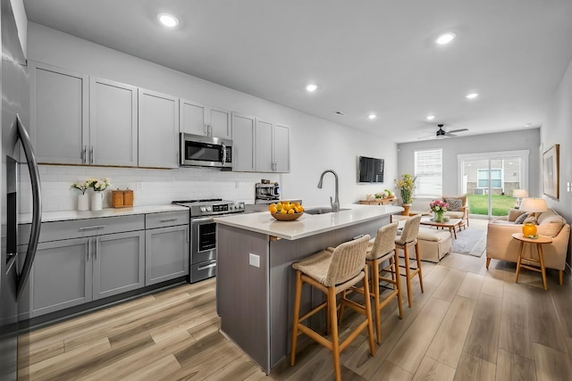 kitchen featuring gray cabinetry, sink, stainless steel appliances, and an island with sink