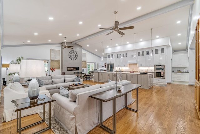 living room featuring a large fireplace, ceiling fan, vaulted ceiling with beams, and light hardwood / wood-style floors