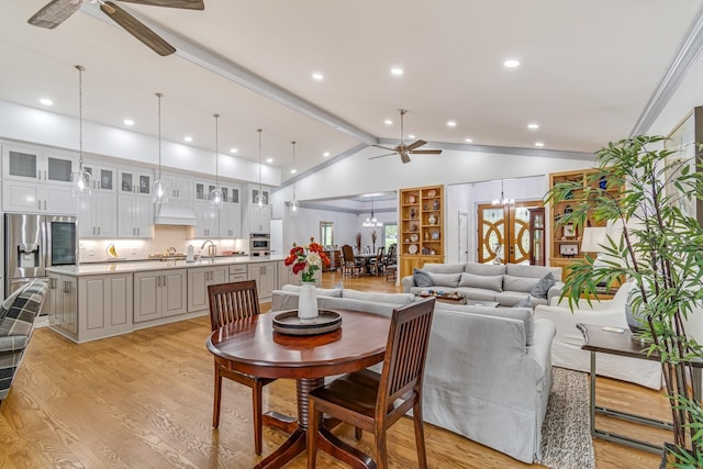 dining area with ceiling fan with notable chandelier, vaulted ceiling, sink, ornamental molding, and light wood-type flooring