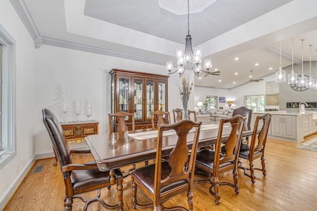 dining space with crown molding, light hardwood / wood-style floors, a notable chandelier, and a raised ceiling