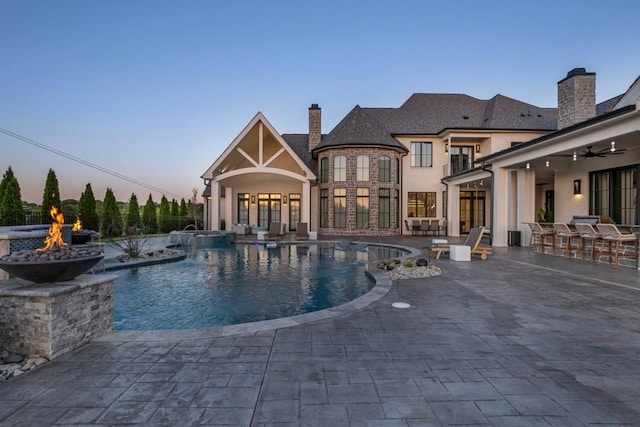 pool at dusk featuring a patio area, a pool with connected hot tub, an outdoor fire pit, and ceiling fan
