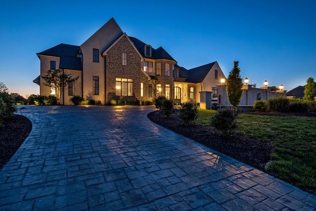 view of front facade featuring stucco siding, stone siding, a lawn, and curved driveway