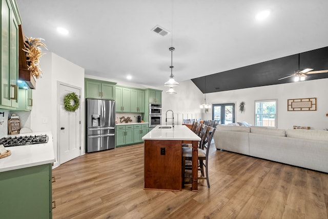 kitchen with light hardwood / wood-style flooring, decorative light fixtures, green cabinetry, stainless steel appliances, and an island with sink