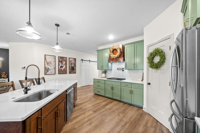 kitchen featuring sink, pendant lighting, a barn door, light hardwood / wood-style flooring, and appliances with stainless steel finishes