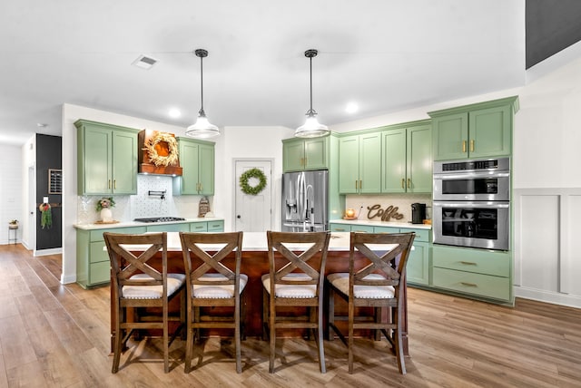 kitchen with light hardwood / wood-style flooring, green cabinets, decorative light fixtures, decorative backsplash, and appliances with stainless steel finishes