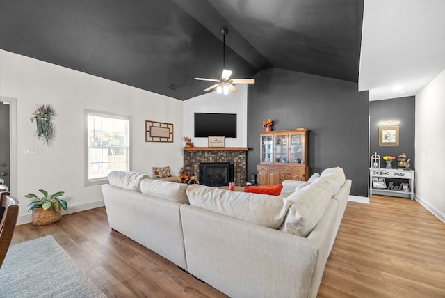 living room featuring ceiling fan, lofted ceiling, a brick fireplace, and light hardwood / wood-style floors