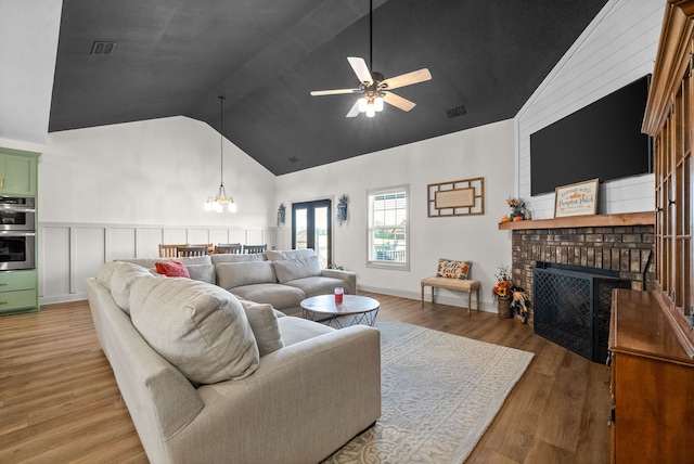 living room featuring wood-type flooring, ceiling fan with notable chandelier, a brick fireplace, and high vaulted ceiling