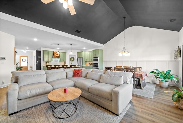 living room featuring ceiling fan with notable chandelier, light hardwood / wood-style flooring, and vaulted ceiling