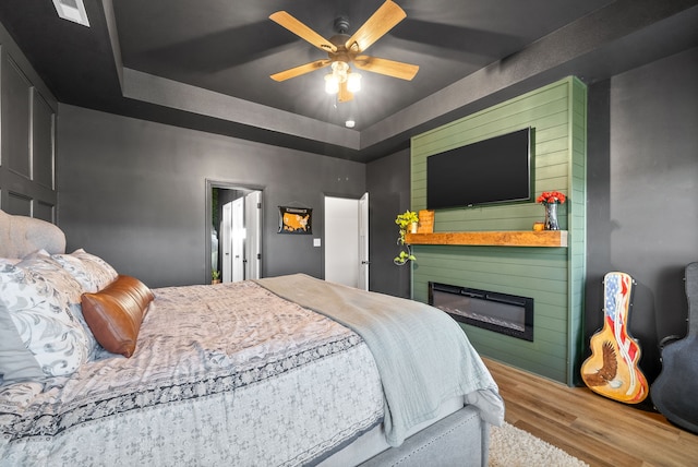 bedroom with ceiling fan, a raised ceiling, and hardwood / wood-style floors