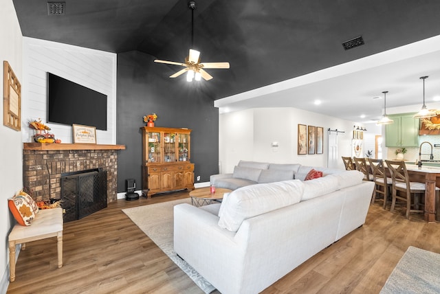 living room with ceiling fan, wood-type flooring, vaulted ceiling, sink, and a fireplace