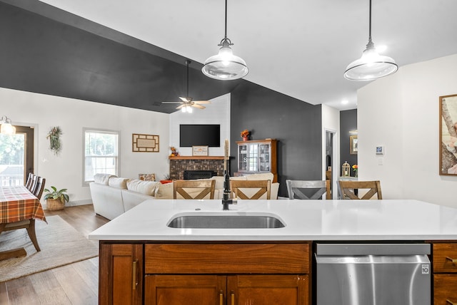 kitchen featuring ceiling fan, stainless steel dishwasher, sink, a fireplace, and light hardwood / wood-style flooring