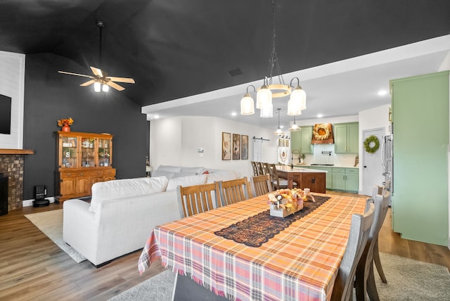 dining space with high vaulted ceiling, sink, light hardwood / wood-style floors, ceiling fan with notable chandelier, and a fireplace