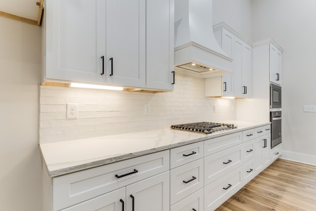 kitchen featuring custom exhaust hood, white cabinets, light hardwood / wood-style flooring, light stone counters, and stainless steel appliances