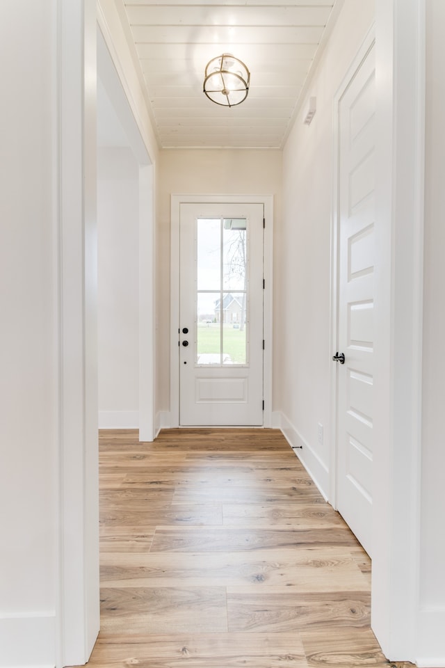 doorway to outside featuring light hardwood / wood-style flooring, wooden ceiling, and crown molding