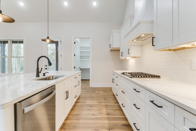 kitchen featuring appliances with stainless steel finishes, custom exhaust hood, sink, white cabinetry, and hanging light fixtures