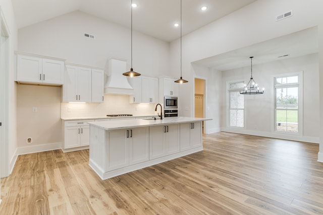 kitchen with premium range hood, white cabinetry, a kitchen island with sink, and light hardwood / wood-style floors