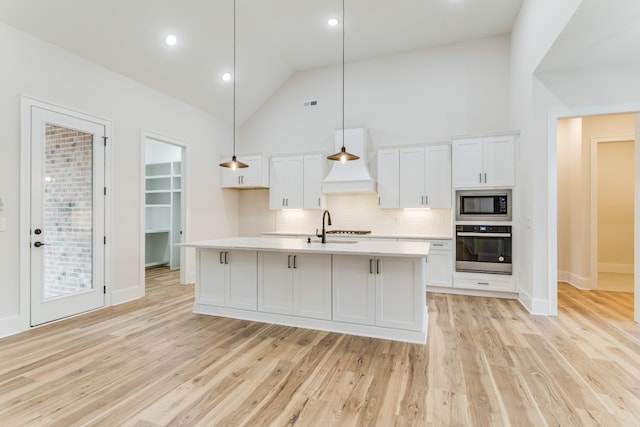 kitchen with black microwave, oven, hanging light fixtures, and an island with sink